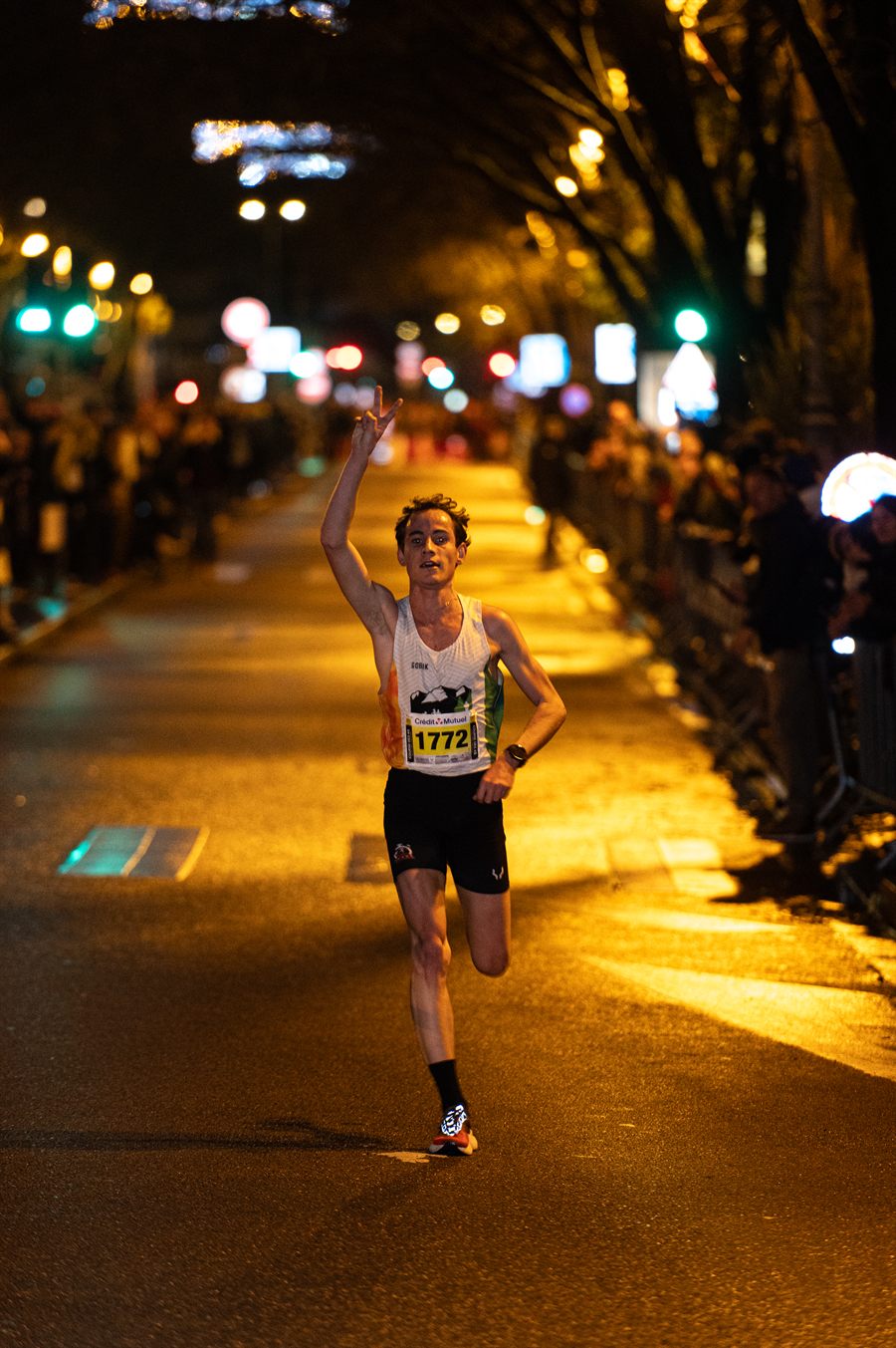 Un coureur élite lève le bras à l'arrivée, sous les lumières